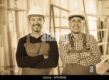 Two positive specialists in helmets and workwear posing at workshop Stock Photo