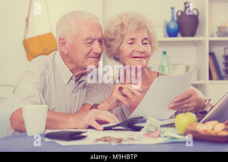 Smiling senior couple sitting at table counting home finances with laptop Stock Photo