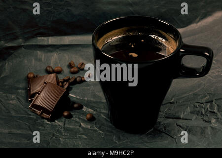 Black coffee mug with beats of chocolate against a black moody background. Stock Photo