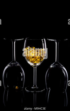 Three wine glasses with yellow pills against a black elegant background. Stock Photo