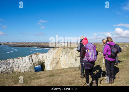 Hikers looking at Bwa Gwyn / White Arch natural rock formation on Isle of Anglesey Coastal Path on seacliffs. Rhoscolyn Anglesey Wales UK Stock Photo