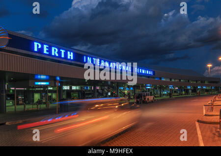 An external dusk view of Perth International Airport in Western Australia. A blurred car moves across frame in the foreground. Stock Photo