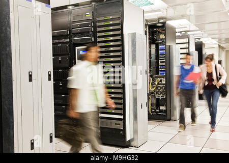 Three multi-ethnic technicians working in a large computer server room. Stock Photo