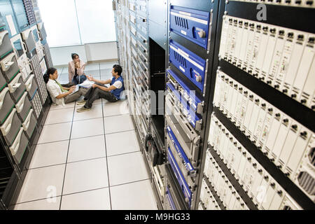 Three multi-ethnic technicians working in a large computer server room. Stock Photo