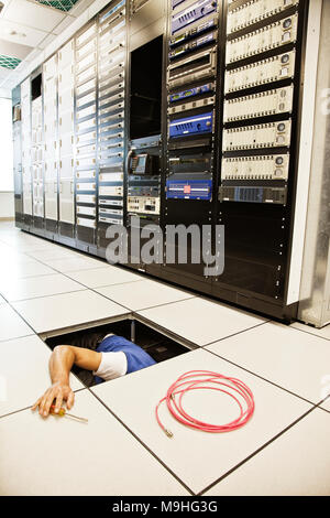 Computer technician working on wiring systems in the floor of a large computer server room Stock Photo