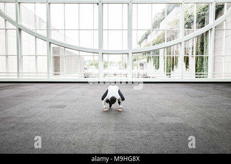 Businessman relaxing doing a yoga pose in a large open glass covered walkway. Stock Photo
