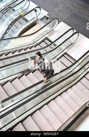 Mixed race pair of business people on the way to a meeting near a set of escalators. Stock Photo