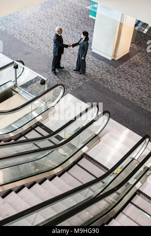 Mixed race pair of business people on the way to a meeting near a set of escalators. Stock Photo