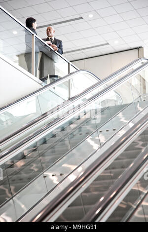 Mixed race pair of business people on the way to a meeting near a set of escalators. Stock Photo
