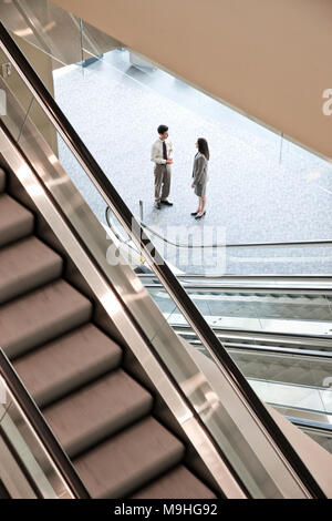 Mixed race pair of business people on the way to a meeting near a set of escalators. Stock Photo