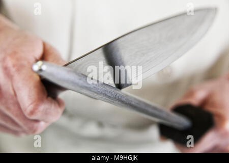 Close-up of a chef sharpening a large kitchen knife blade with a steel. Stock Photo