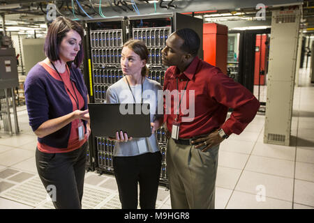 Mixed race group of technicians doing diagnostic tests on servers in a large server farm. Stock Photo