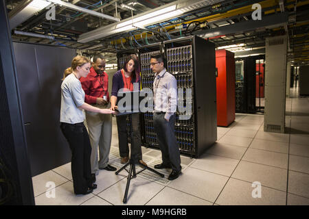 Mixed race group of technicians doing diagnostic tests on servers in a large server farm. Stock Photo