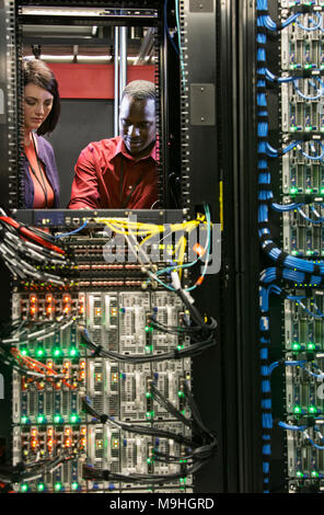 Caucasian woman and black man technicians running diagnostic tests on servers in a large computer server farm. Stock Photo