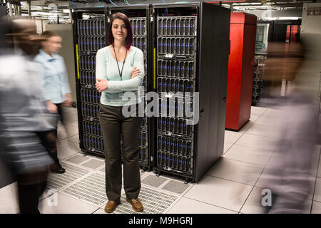 Caucasian woman technician standing in an aisle of a large computer server farm. Stock Photo