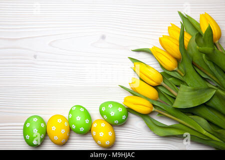Easter eggs and yellow tulips on white wooden background. Stock Photo