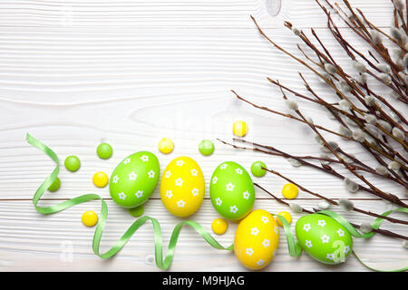 Easter eggs, chocolate candies and willow branches on white wooden background. Stock Photo