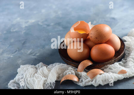 Fresh chicken eggs in a wooden bowl on a concrete background with white cloth. Organic ingredients concept with copy space. Stock Photo