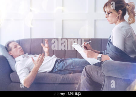Serious calm therapist taking notes Stock Photo