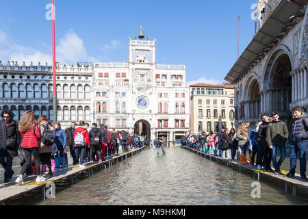 Two lines of people on passarelles during Acqua Alta (high tide flooding), Piazza San Marco (St Marks Square), Venice, Veneto,  Italy with the Clock T Stock Photo