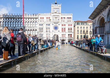 People walking on passarelles in Piazza San Marco (St Marks Square) during Acqua Alta flooding including a young boy in a wheelchair, Venice, Veneto,  Stock Photo