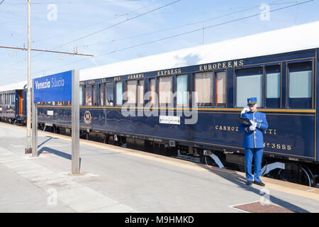The Venice Simplon Orient-Express  luxury train in Venezia S Lucia station, Venice, Veneto,  Italy with a staff member waiting to welcome passengers Stock Photo