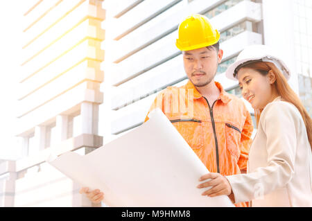 engineer and foreman looking at constructed paper blueprint plans at construction site. Stock Photo