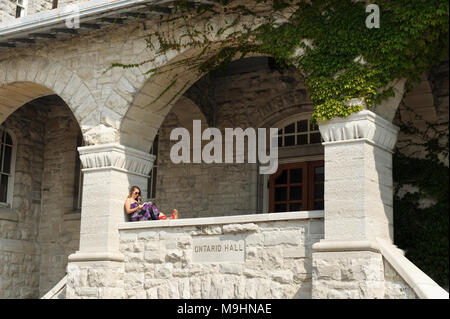 A young woman reads a book, sitting on the porch of Ontario Hall Building, Queen's University, Kingston, Ontario, Canada. Stock Photo