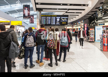 Group of air passengers at Heathrow Airport Terminal Five watching the departures board on a day when many flights had been cancelled or delayed. Stock Photo