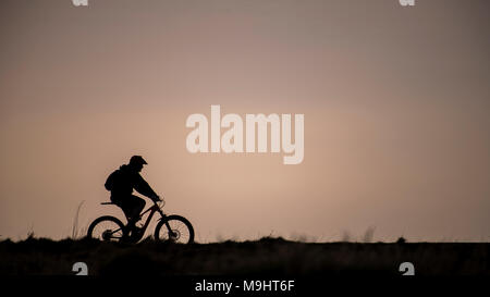 A mountain biker silhouetted against the evening sky in Cumbria. Stock Photo