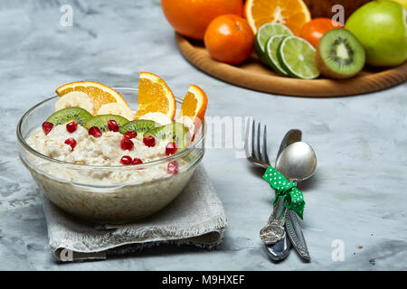 Breakfast still life with oatmeal porridge and fruits served with fork, spoon on homespun napkin over wooden background, top view, selective focus, sh Stock Photo