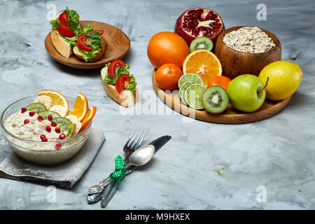 Breakfast still life with oatmeal porridge and fruits served with fork, spoon on homespun napkin over wooden background, top view, selective focus, sh Stock Photo