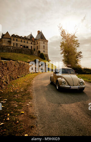 A classic VW Beetle drives past the Château de Biron a castle in the valley of the Lède in the commune of Biron in the Dordogne France. Stock Photo