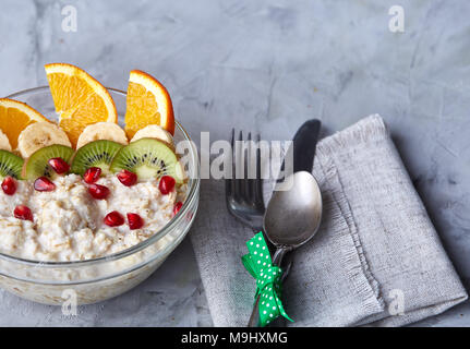 Breakfast still life with oatmeal porridge and fruits served with fork, spoon on homespun napkin over wooden background, top view, selective focus, sh Stock Photo