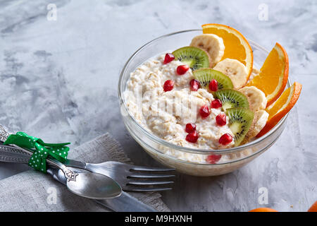 Breakfast still life with oatmeal porridge and fruits served with fork, spoon on homespun napkin over wooden background, top view, selective focus, sh Stock Photo