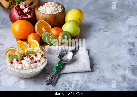 Breakfast still life with oatmeal porridge and fruits served with fork, spoon on homespun napkin over wooden background, top view, selective focus, sh Stock Photo