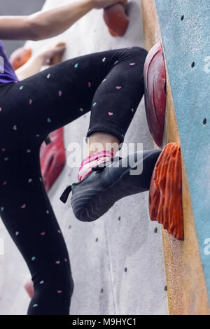 Girl climbing up on wall in gym, focus on feet Stock Photo