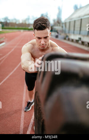 Close-up of young muscular man flipping a huge tire for training muscles at the tartan track on the stadium. Stock Photo