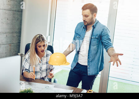 Young worried architect colleagues talking and analyzing blueprints while working on a new project at the office. Stock Photo