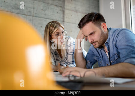 Young worried architect colleagues talking and analyzing blueprints while working on a new project at the office. Stock Photo