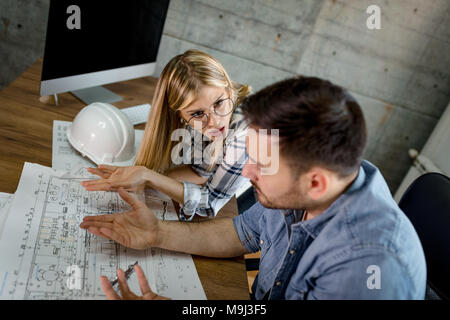 Young worried architect colleagues talking and analyzing blueprints while working on a new project at the office. Stock Photo