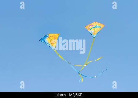 Two colourful kites flying against a cloudless blue sky. Stock Photo