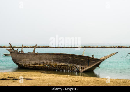 an old and broken abandoned wooden fishing ship is wiped out from the sea and kept on the sandy beach in cloudy weather and greenish water of the sea
