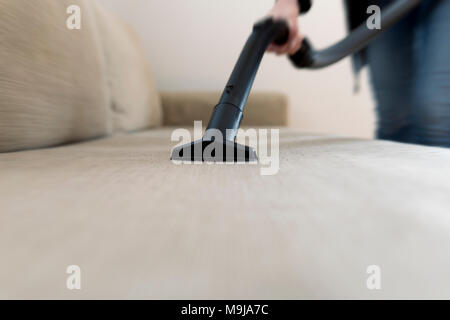Woman cleaning the sofa, couch with vacuum cleaner Stock Photo