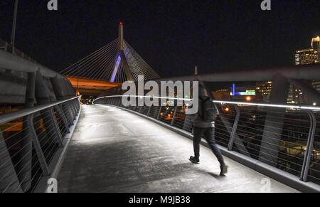 Boston, Massachusetts, USA. 25th March, 2018. On a cold, spring night, a pedestrian walks the well-lit North Bank Bridge in Boston, a pedestrian bridge connecting Boston's North Point Park to Paul Revere Park in Cambridge. Credit: Andrew Cline/Alamy Live News Stock Photo