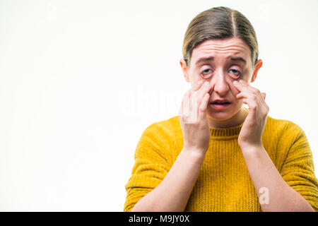 A young Caucasian woman girl feeling and looking unwell sick hungover,  pulling her eyelids down, shot against a white background, UK Stock Photo