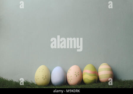 A row of decorated eggs in different colours on artificial grass against blue grey background for Easter. Filtered to give muted, retro style. Stock Photo