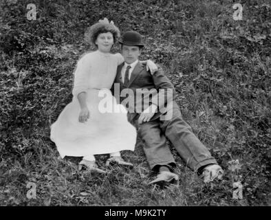 Young couple lounge in a grassy field, ca. 1910. Stock Photo