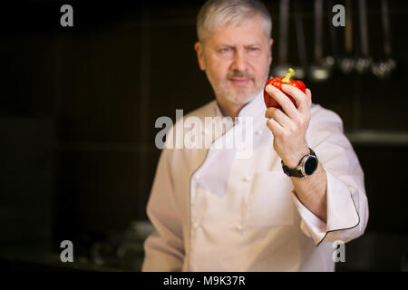 old chef with white hair and beard standing with red pepper. choose fresh vegetables. Stock Photo