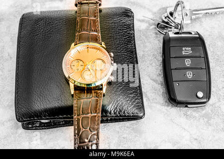 an expansive and stylish brand new set of a black shining leather wallet and a watch with a remote car key kept on a marble floor Stock Photo